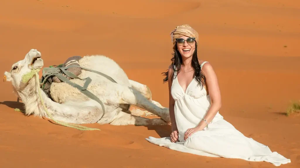 Traveler posing beside a white camel during a professional photoshoot in the Erg Chebbi dunes of Merzouga, Morocco.