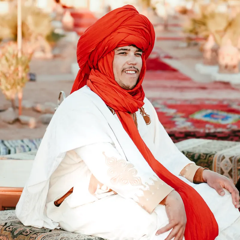 Local Merzouga desert guide wearing traditional Amazigh clothing and a red turban in the Sahara.