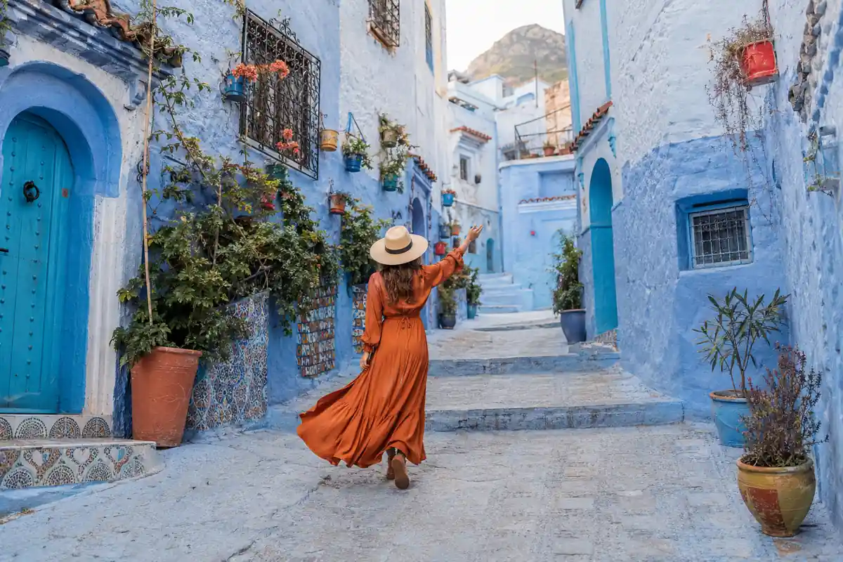 Woman in an orange dress exploring the blue streets of Chefchaouen during a private Morocco tour.